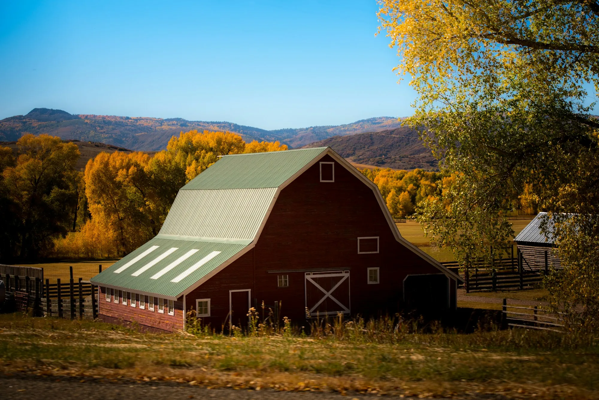 Red barn with a green roof surrounded by fall trees and hills