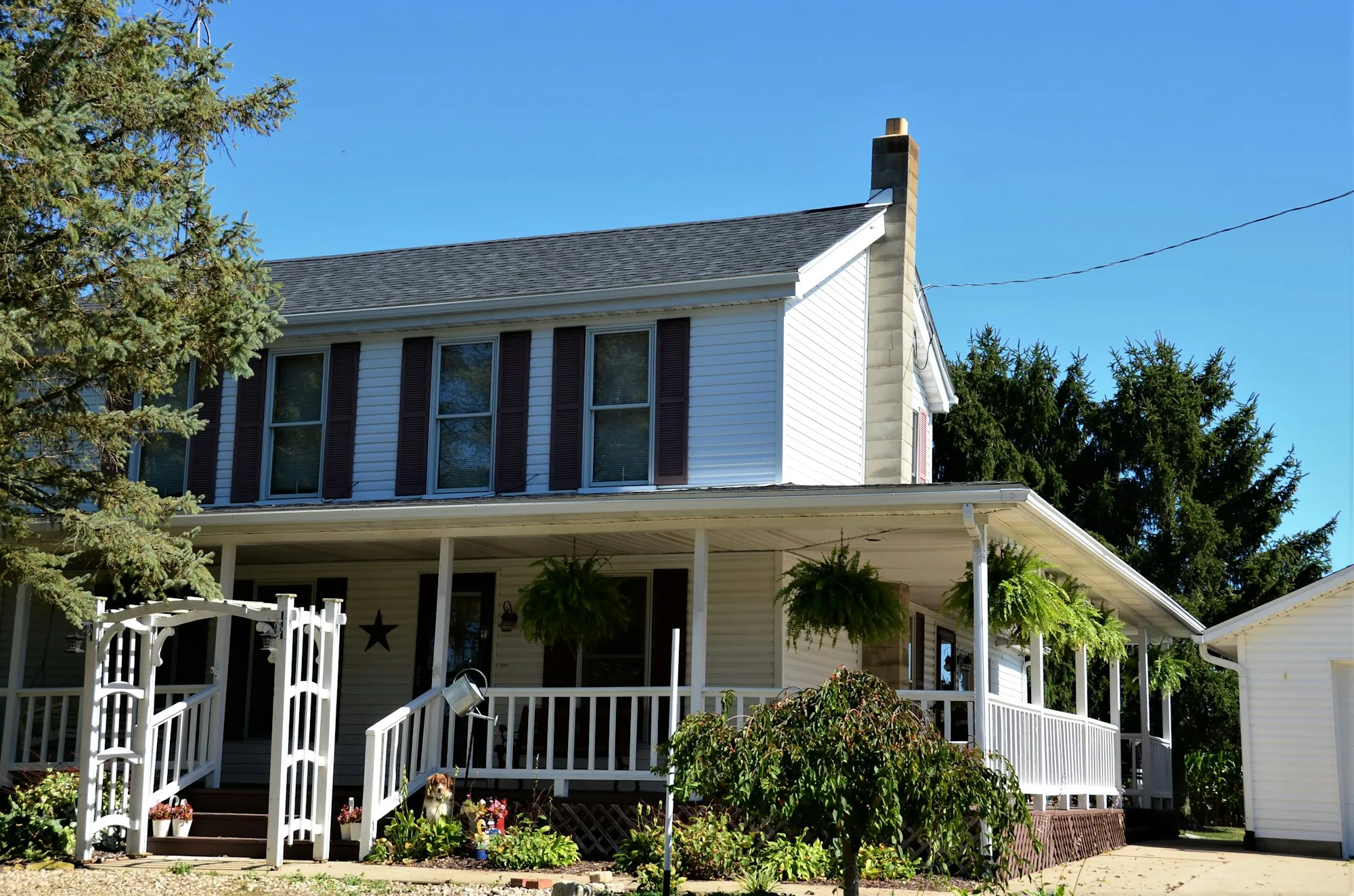 White two-story farmhouse with a covered front porch and garden arbor