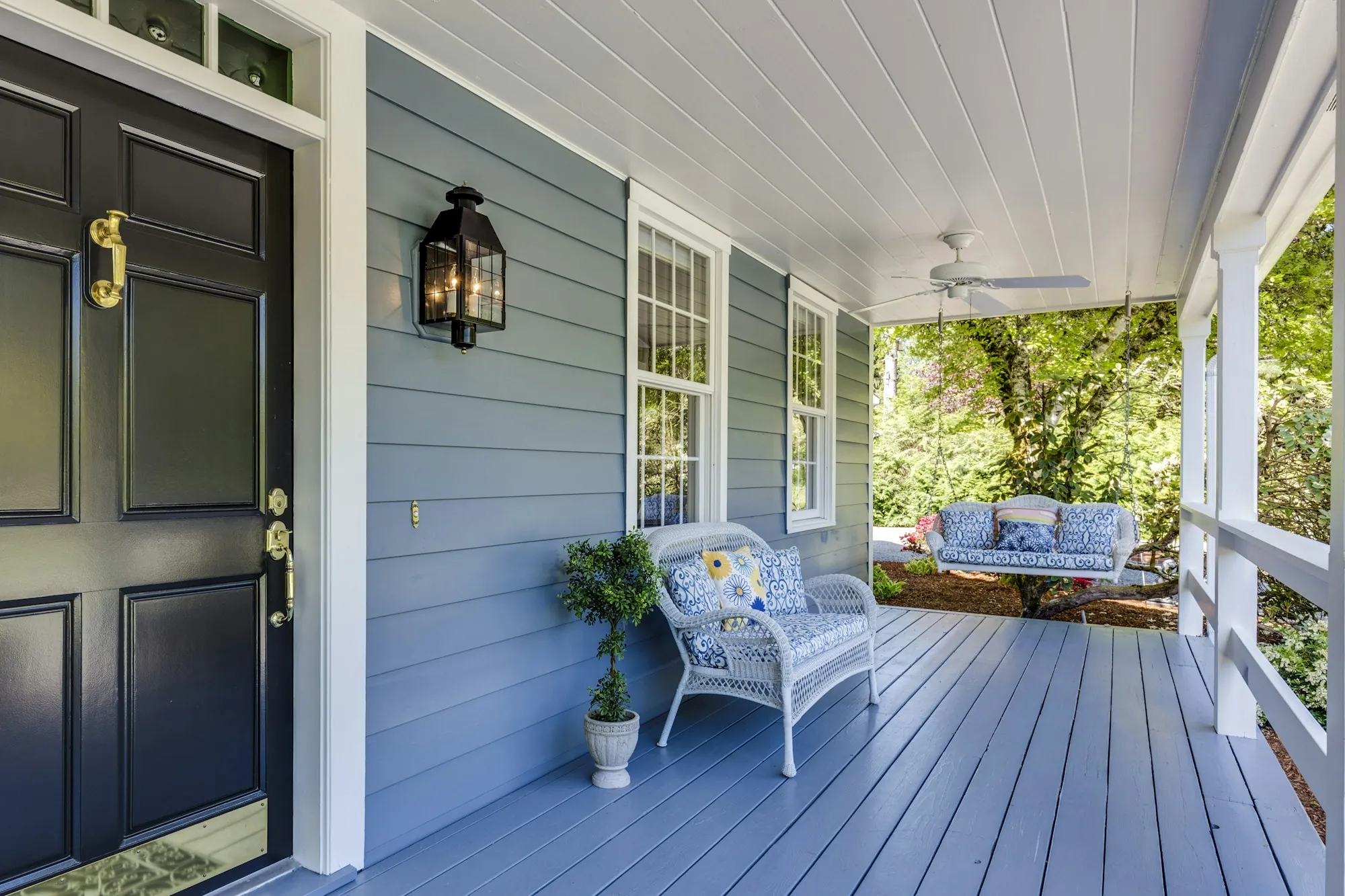 Dark front door on a light blue painted porch with white wicker seating
